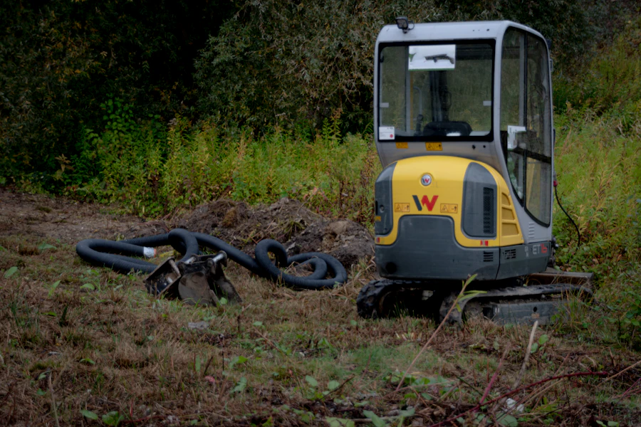 Compact excavator parked beside coiled drainage pipe at the edge of a field