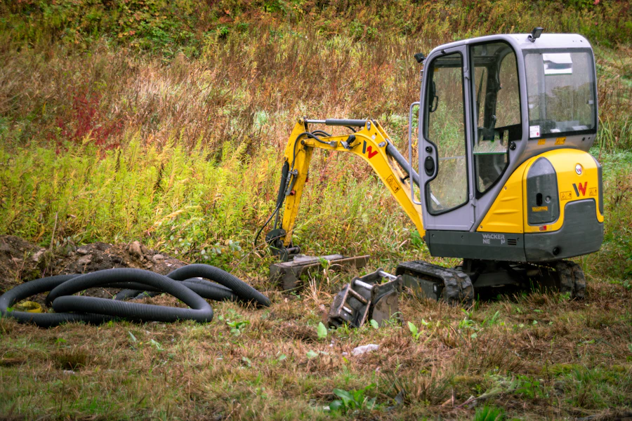 Compact excavator beside coils of drainage pipe on a grassy slope